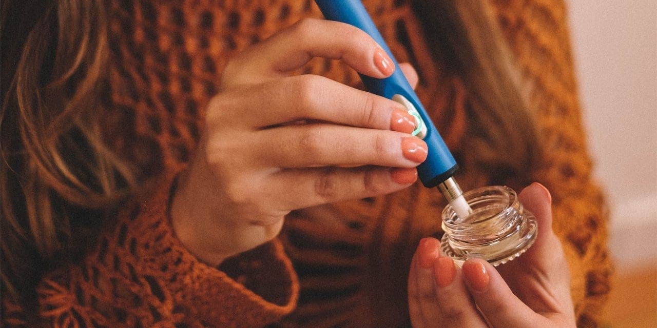 close-up of a woman's hands using a dab pen with a wax concentrate