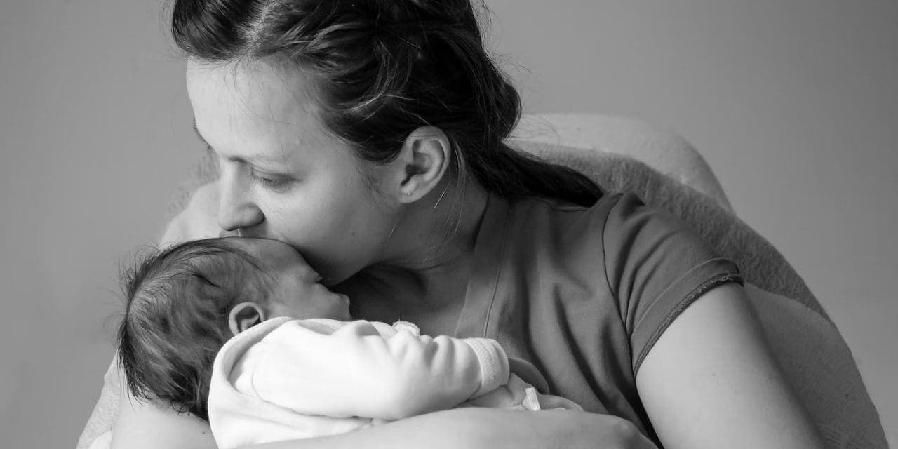 Una madre lleva y besa en la frente a su bebé recién nacido